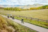 A family of four rides their bikes down a paved path in a green mountain valley.