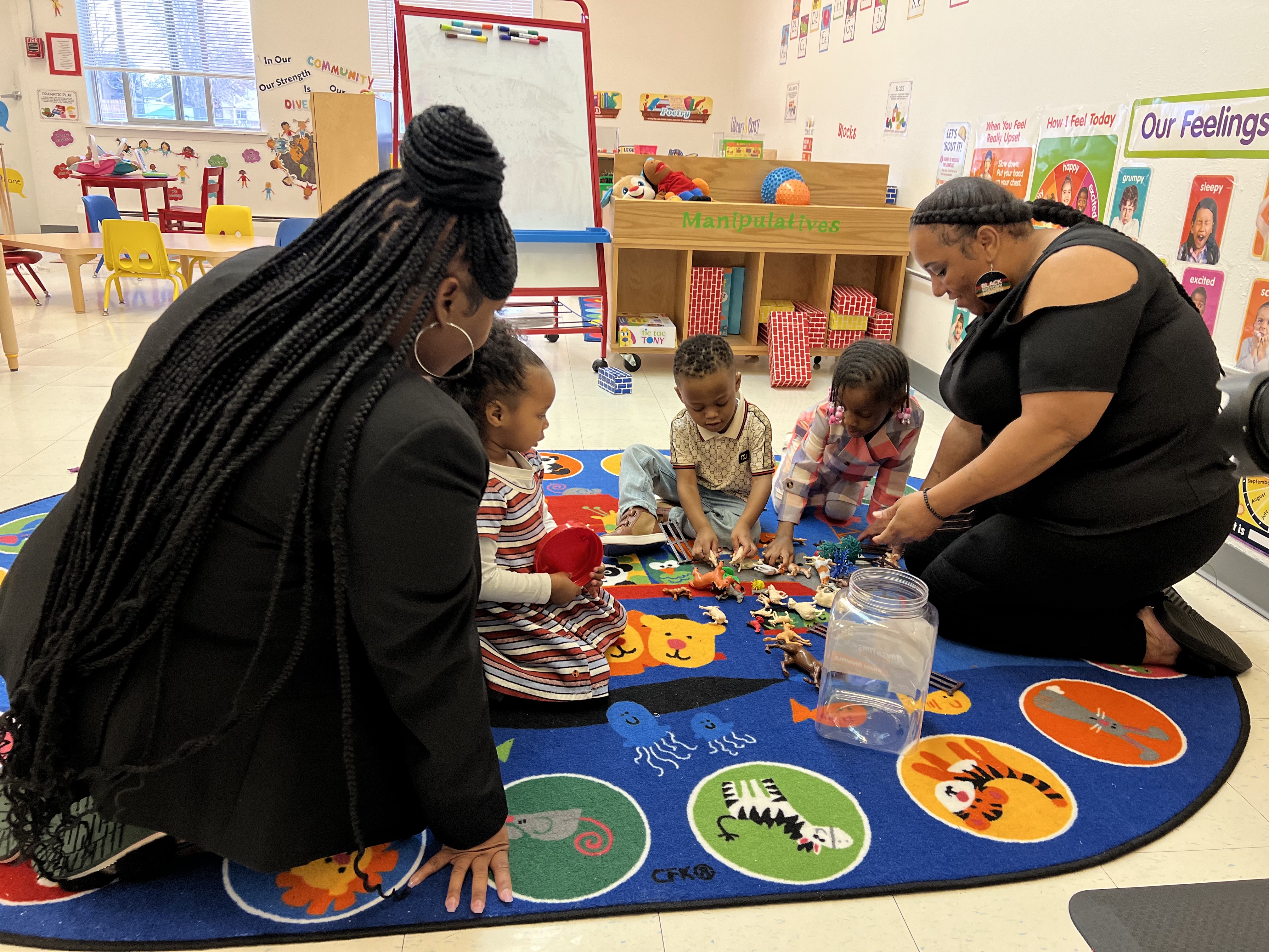 Photo of two caretakers playing with three children in a classroom