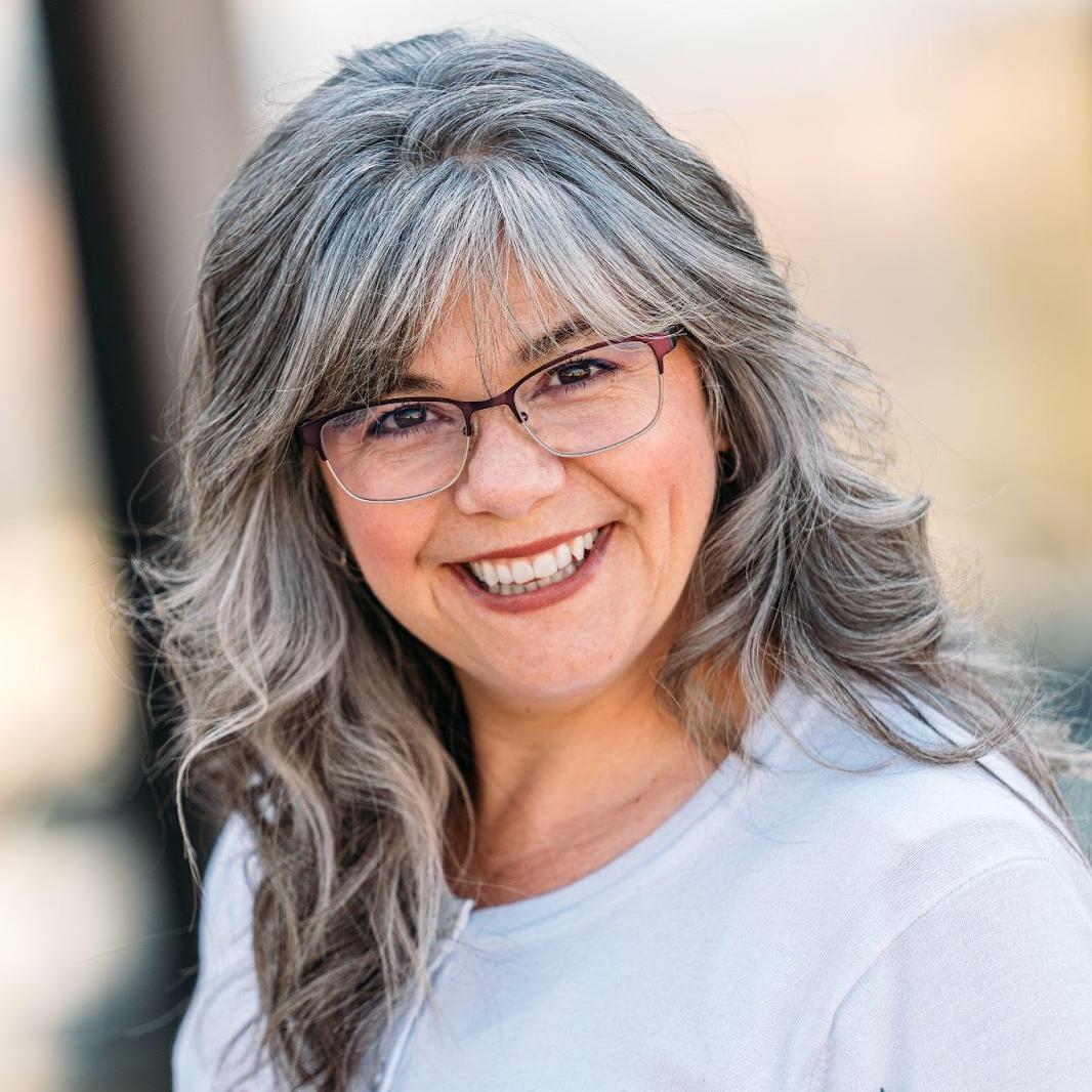 Woman wearing a white button down, glasses, and is smiling.