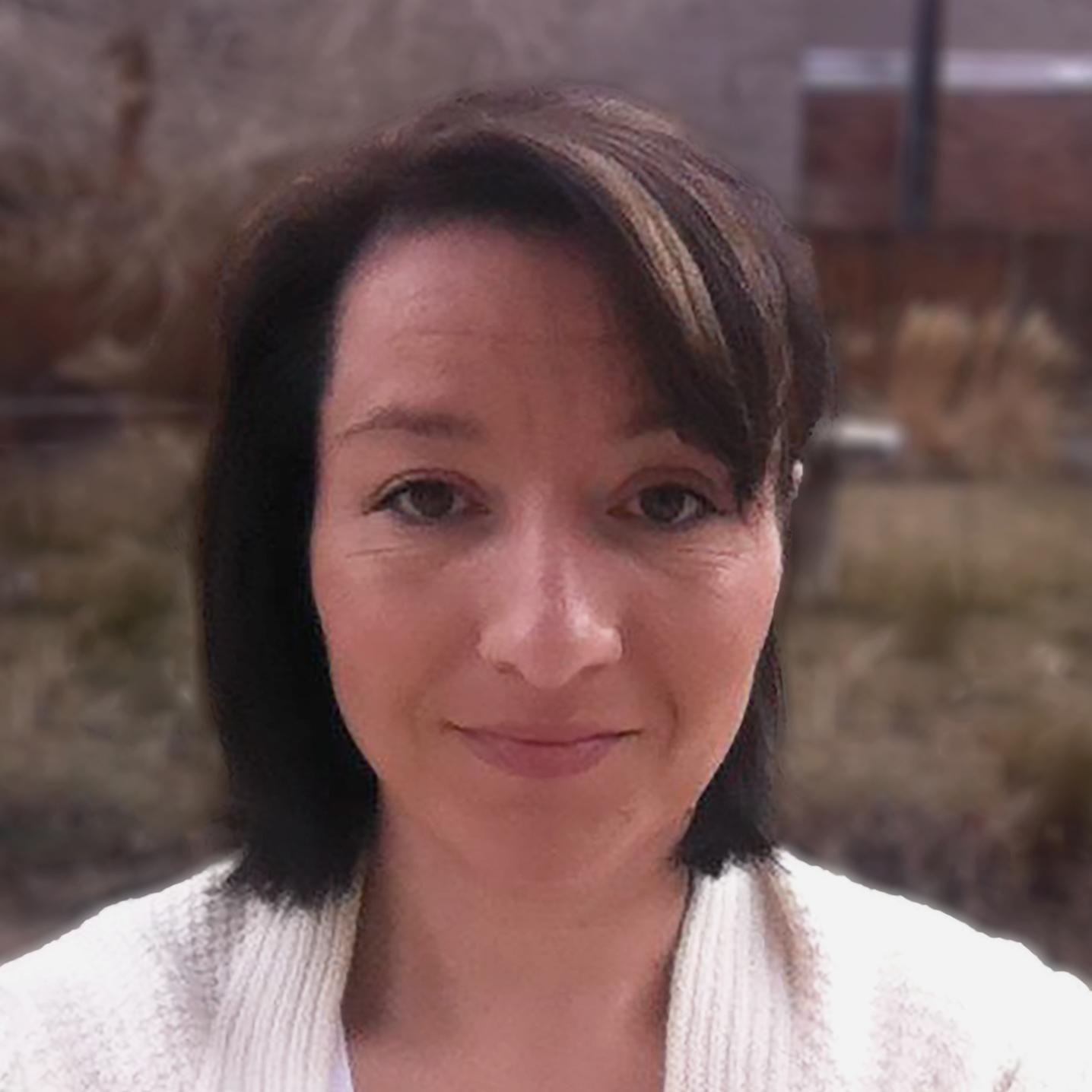 Woman with dark brown hair smiling with her mouth closed, wearing a cream cardigan and white vneck t-shirt.