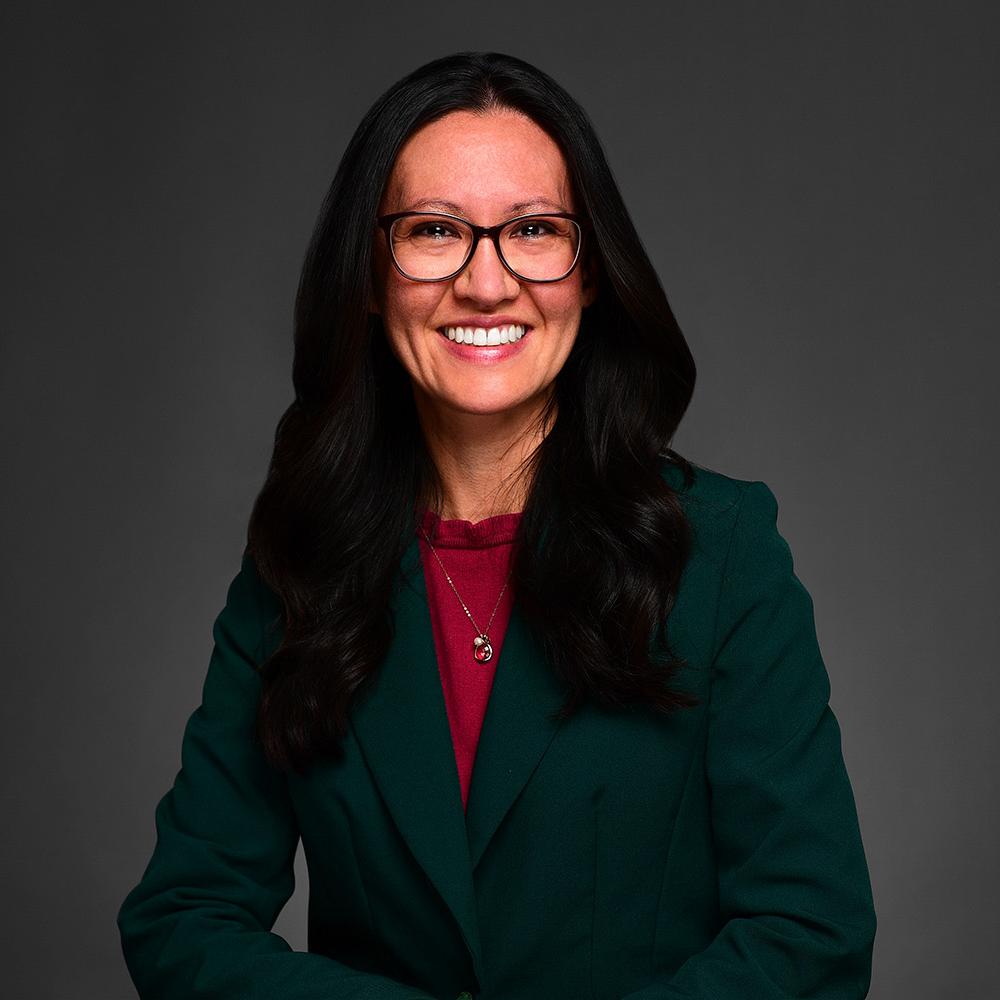 Headshot of Christina Tuchman. She is wearing a dark green blazer with long brown hair. 