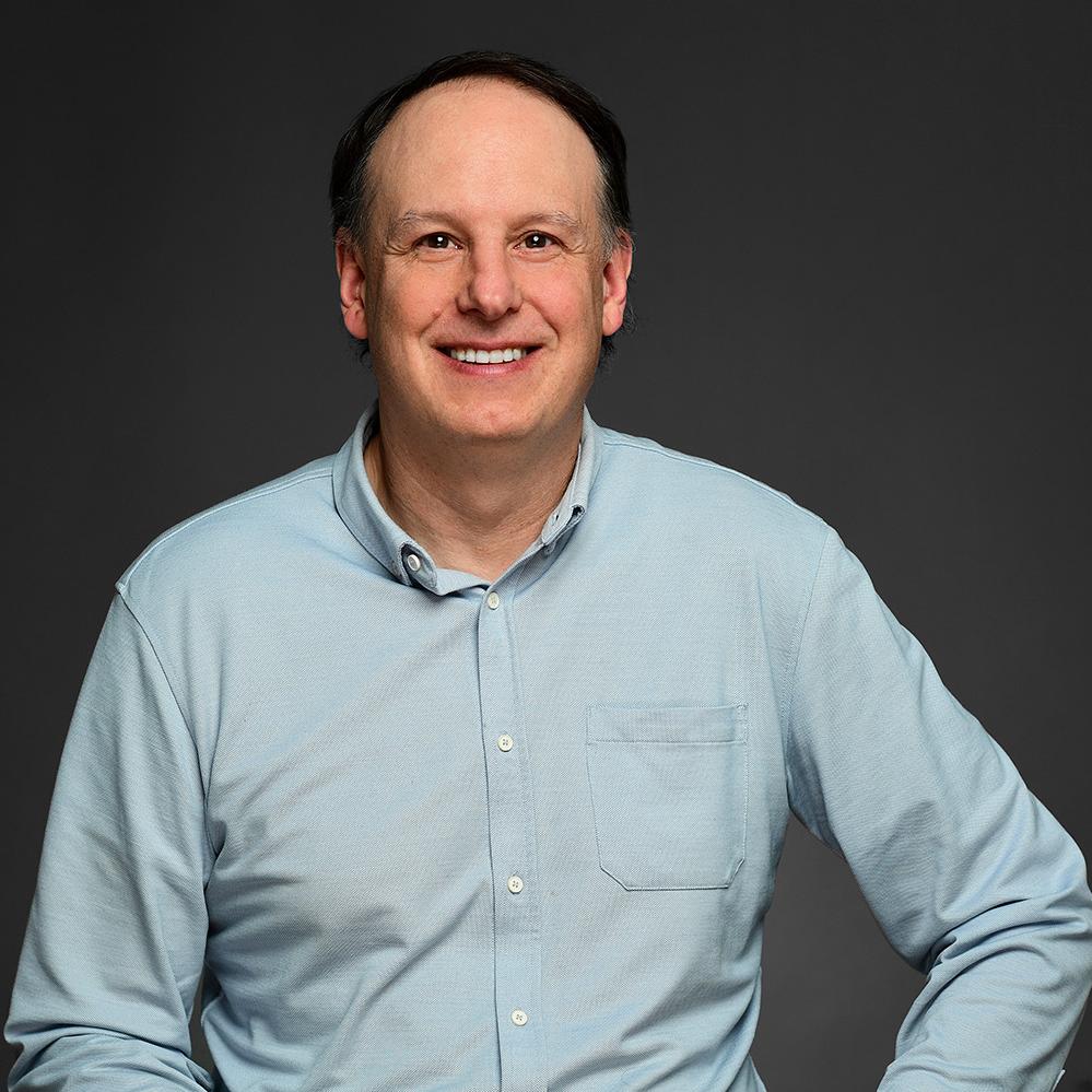 Headshot of Jeff Kraft wearing a light blue collard shirt. He is smiling and has dark brown hair. 