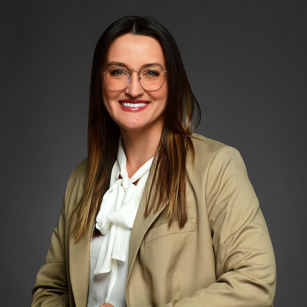 Headshot of Morgan Vankat. She is wearing a glasses, beige business jacket, a white shirt, and a white tie. She has brown hair with lowlights and her hair goes over her shoulders. 