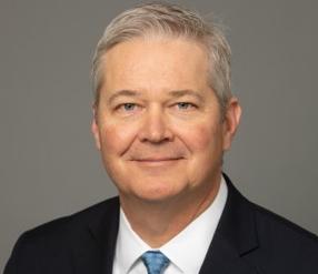 Headshot of Brain Dale, he is wearing grey suit jacket, white shirt, and blue tie.