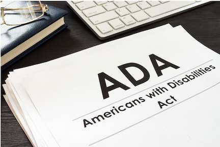 Paperwork entitled 'ADA: Americans with Disabilities Act" on a desktop next to a keyboard, notebook, and reading glasses