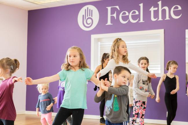 Children pose with arms outstretched in a dance studio with a purple black wall and light wood floors 