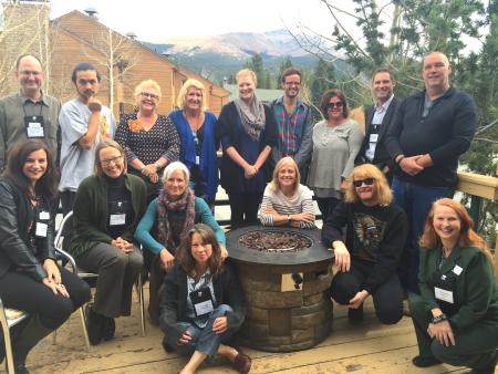 16 change leaders pose around a wooden planter with a mountain vista and cabin style house behind them