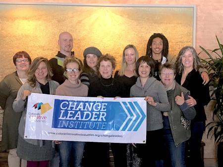11 change leaders pose in a line in front of a golden wall. the front row of the group is holding an official change leader institute poster