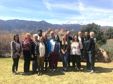 14 change leaders pose in a cluster on a grass lawn with a mountain vista behind them