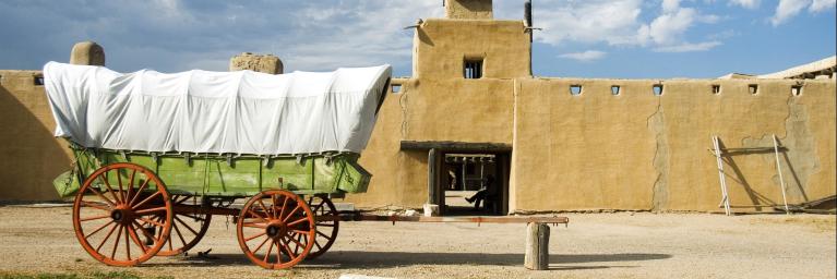 covered wagon in front of pueblo building at Bent's Old Fort