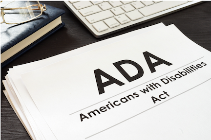 Paperwork entitled 'ADA: Americans with Disabilities Act" on a dark brown desktop next to a keyboard, notebook, and reading glasses