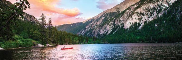 Person paddling a canoe on a lake in front of mountains during sunset in Colorado