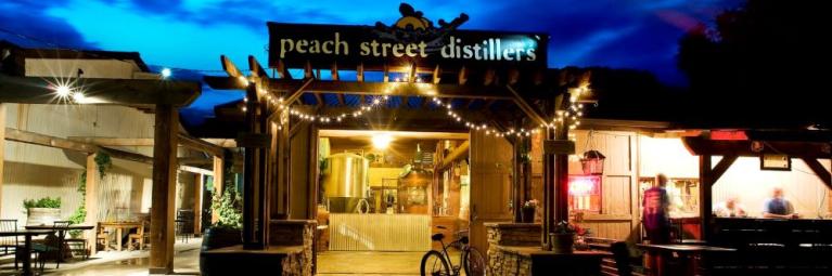 The patio of Peach Street Distillers shines with string lights on a summer evening.