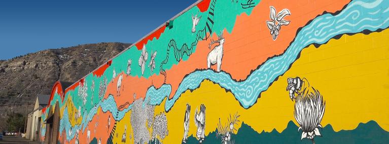 A colorful mural painted on a wall showing a river, train tracks, an elk and other animals.