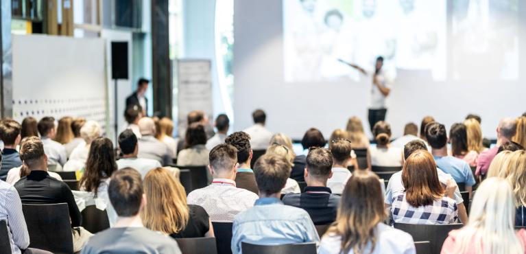 Captivated audience looks to bold speaker giving presentation on a large screen