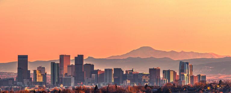 Denver skyline with a pink sunset and mountains in the background