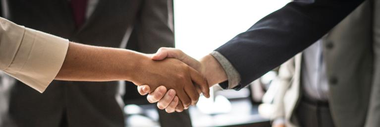 Two business partners shake hand in a conference room.