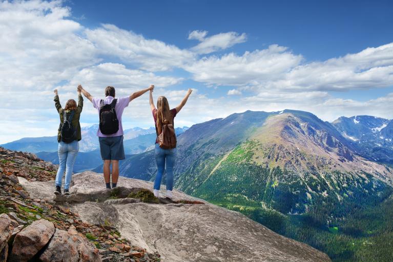 Three hikers stand together at the top of a mountain