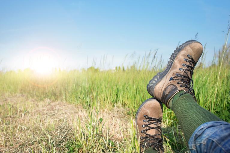 View of a hikers legs and hiking boots with a beautiful grassland and blue sky in the background