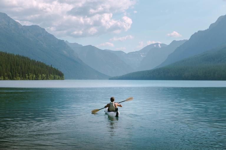 Man kayaks on the water with gorgeous mountains ahead