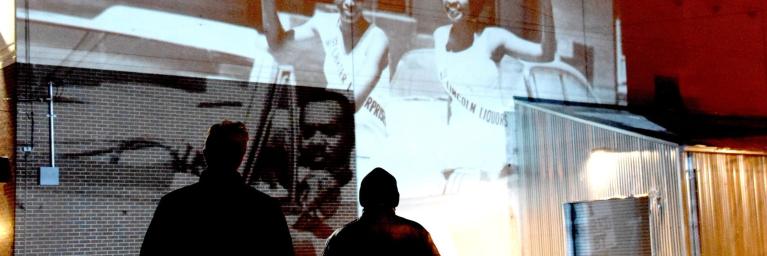 Two people watch a movie projected on the side of a building in RiNo neighborhood of Denver, Colorado for Side Stories film event