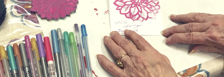 Hands of older adult next to multi colored pens, engaged in art project