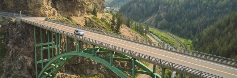 A car drives over an arch bridge over a mountain valley.