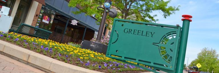 A green sign welcomes visitors to Downtown Greeley.