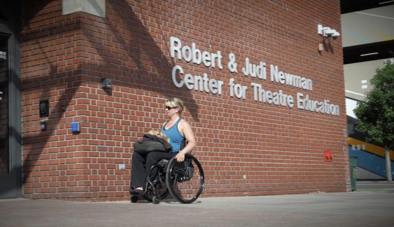 Woman in wheelchair outside of Robert and Judi Newman Center for Theatre Education