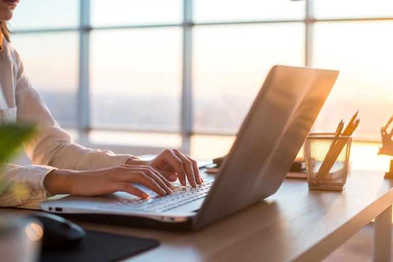 Business woman sits at her desk and works on her laptop as a light shines through