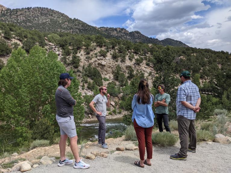 Five members of the Colorado Outdoor Recreation Industry Office meet with business leaders in the mountains with many evergreens in the background