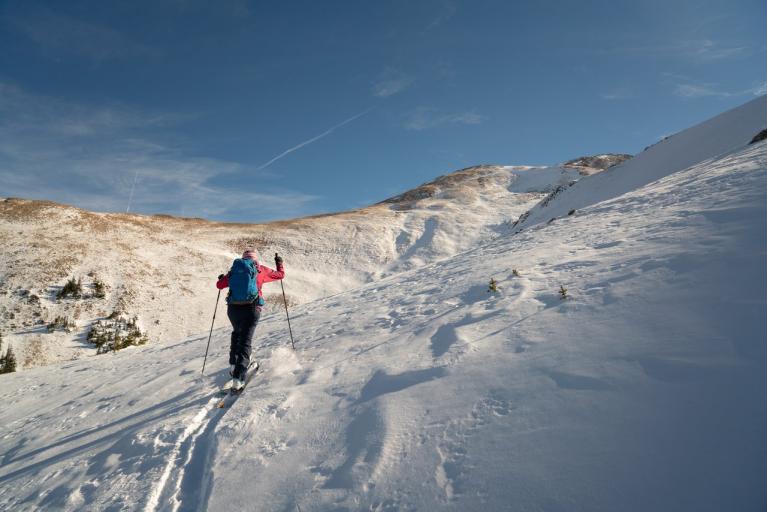 A backcountry skier hikes uphill in the Colorado mountains, with a clear bule sky in the background