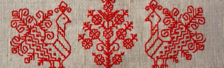 A Russian-style embroidery sample features a red tree with red roosters on either side. 