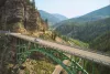A car drives over an arch bridge over a mountain valley.